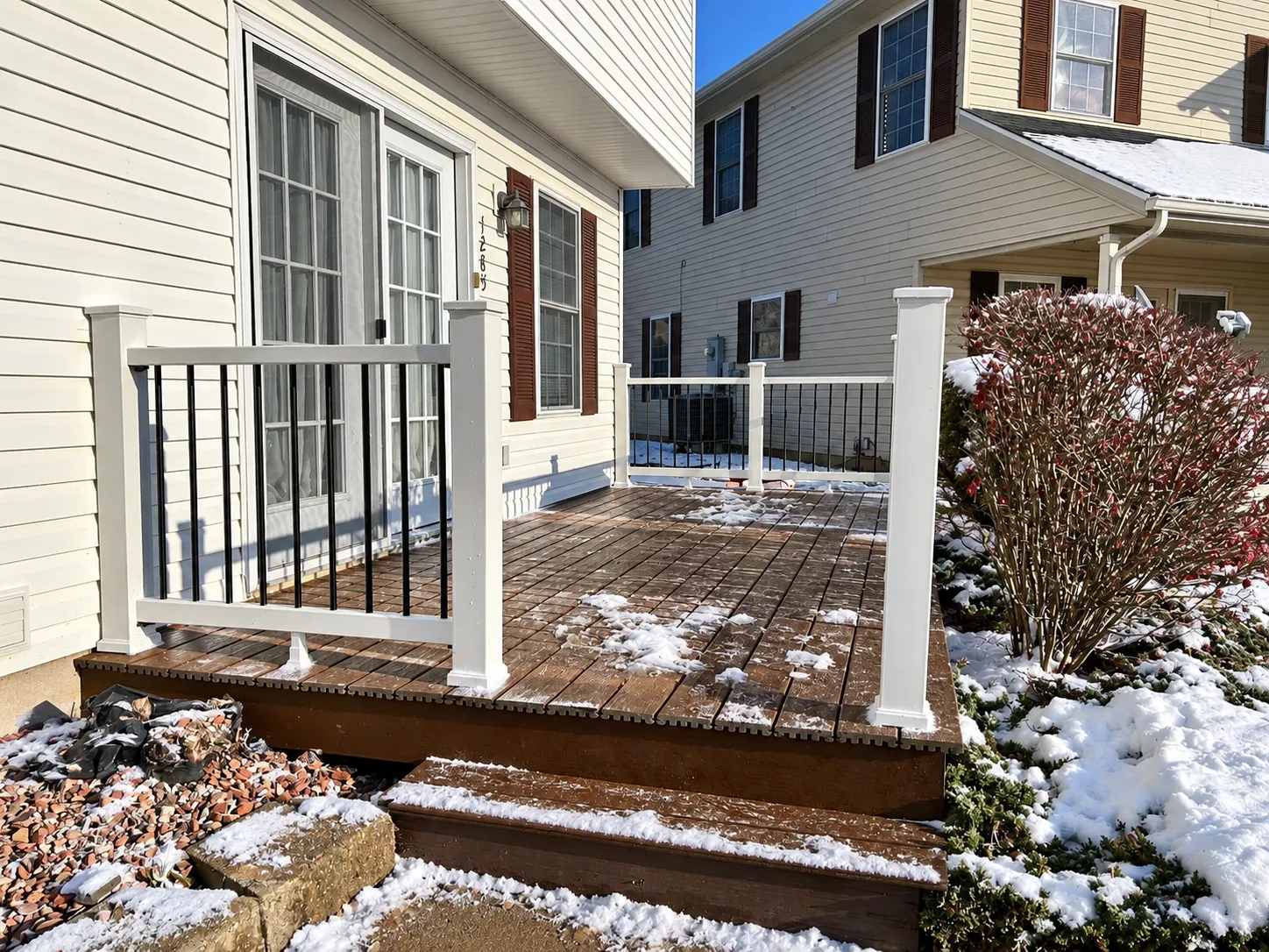 Residential composite deck with white and black railings, showing light snow accumulation on the decking boards and stairs during winter.