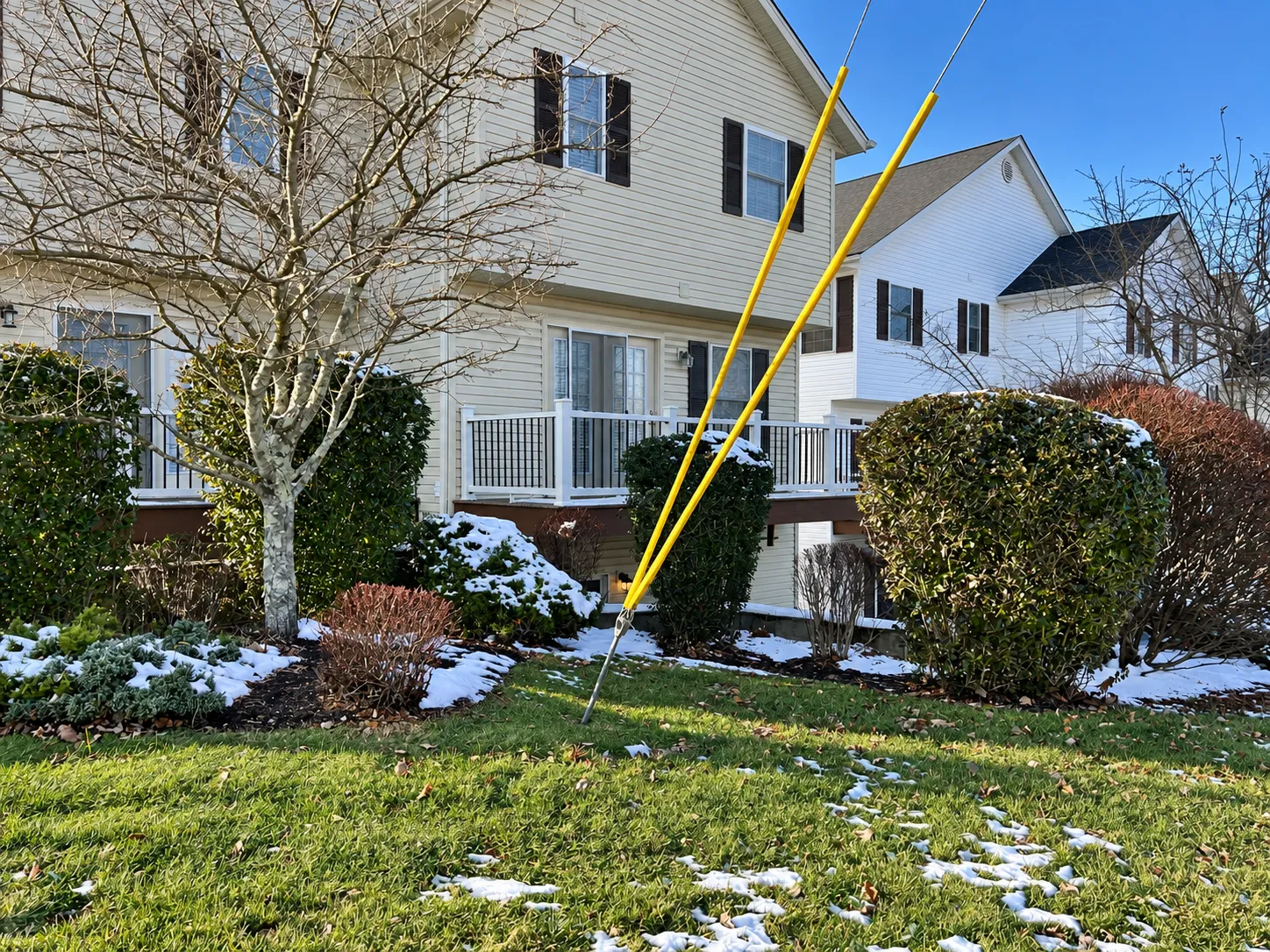Elevated residential deck with white railings and black balusters, surrounded by snow-covered landscaping during winter.