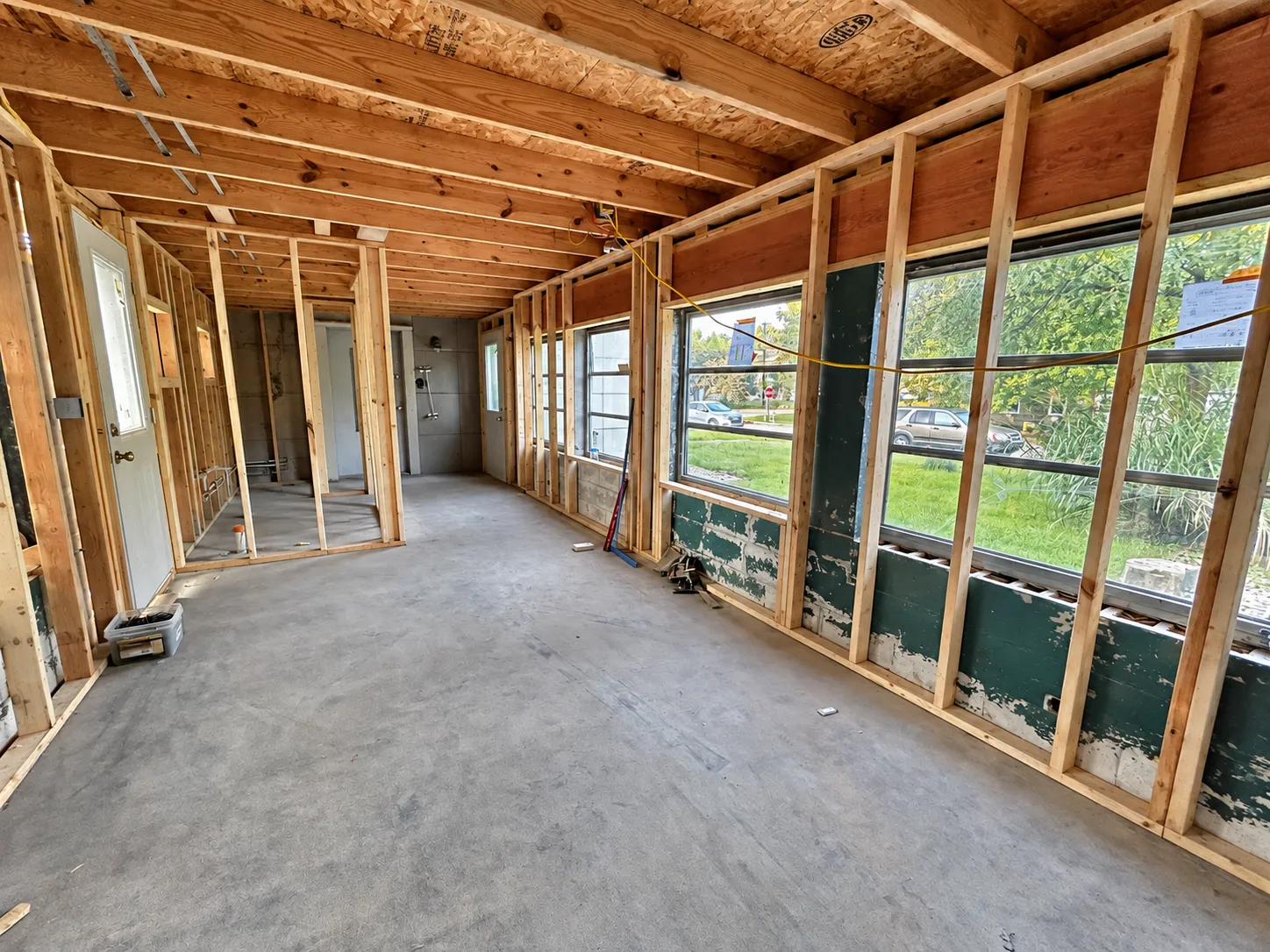 Interior home renovation in progress, featuring exposed wooden wall studs, ceiling joists, and structural framing before drywall installation.
